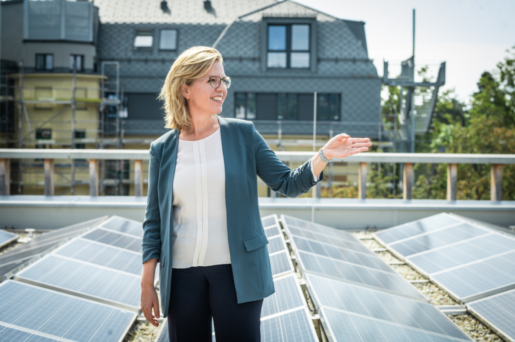 Klimaschutzministerin Leonore Gewessler blickt nach rechts und zeigt mit der linken Hand richtungsweisend in die Zukunft.