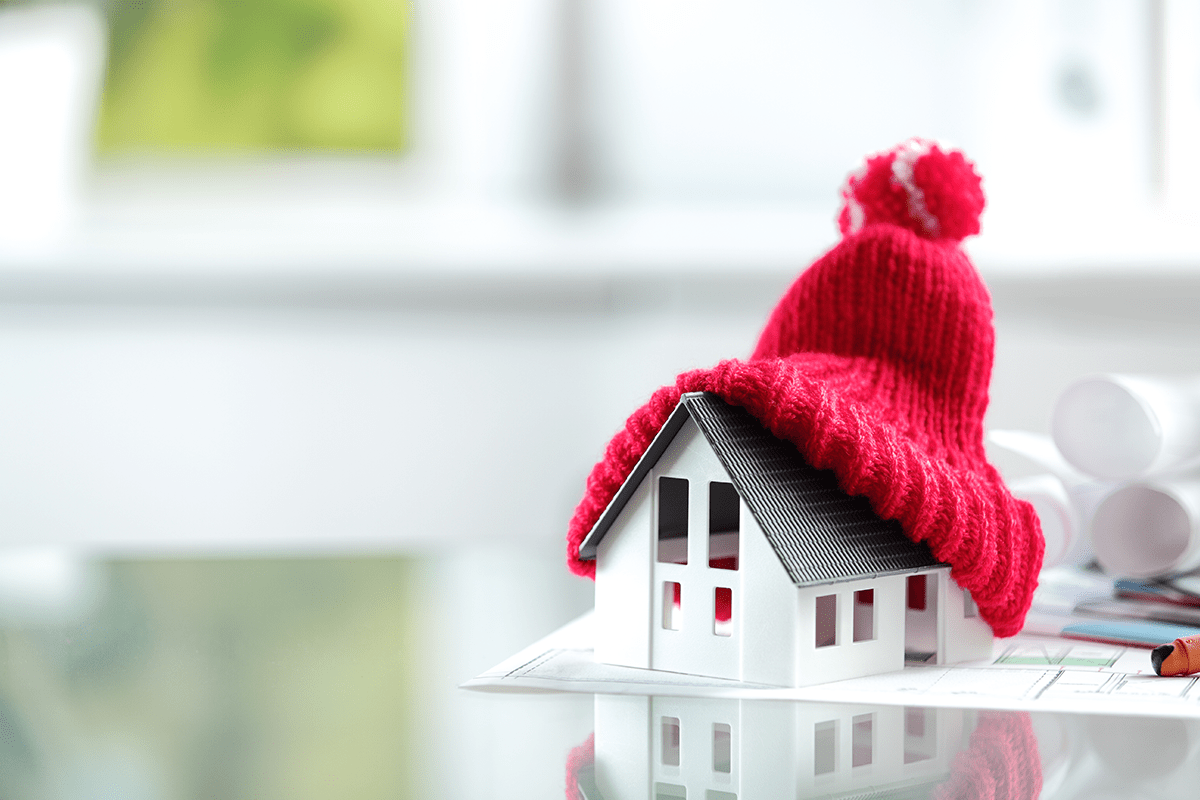 Small white 3-D model house with red woolen cap on an architect's sketch