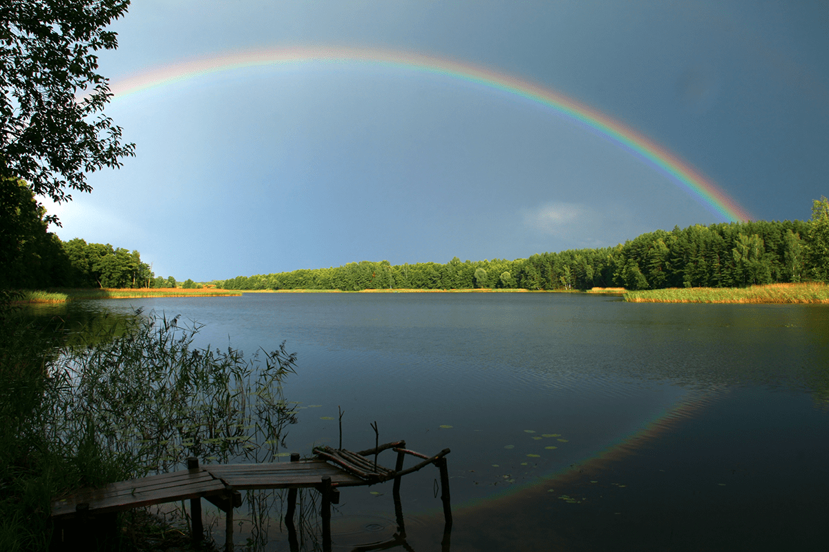 Regenbogen spannt sich von einem Ufer ans andere über einem ruhigen See