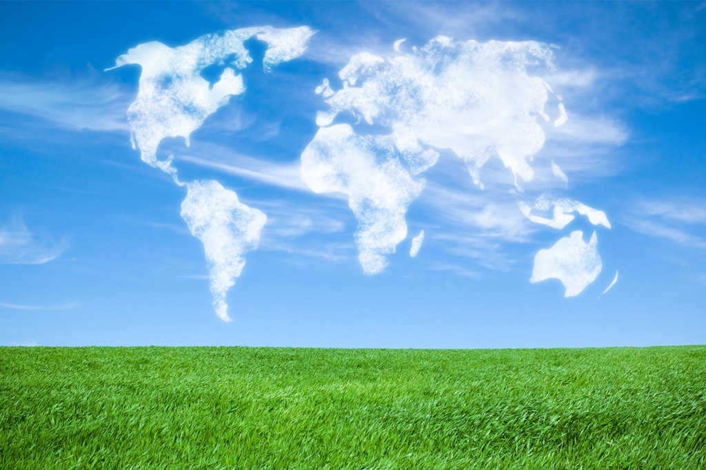 World map shaped from clouds in the blue sky above a meadow